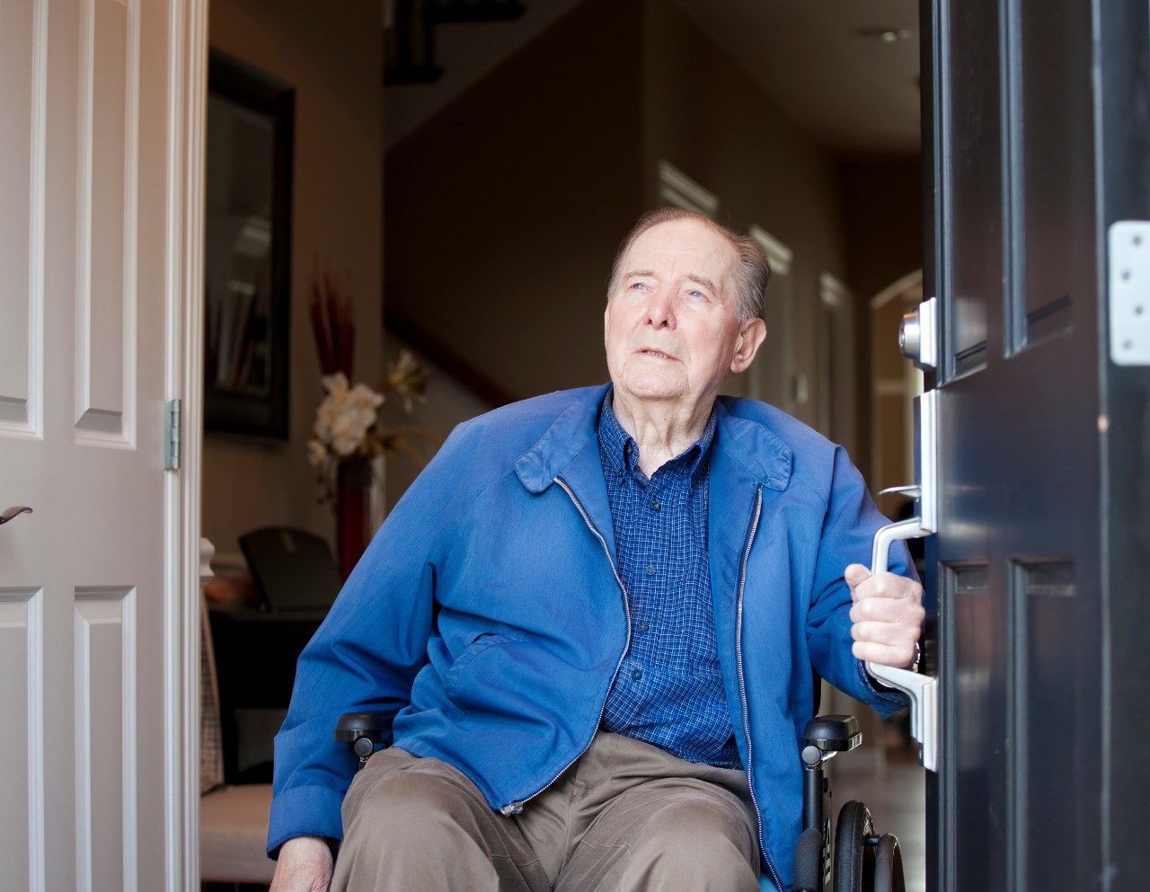Meneer zit in een rolstoel en doet de deur open Meneer zit in een rolstoel en doet de deur open